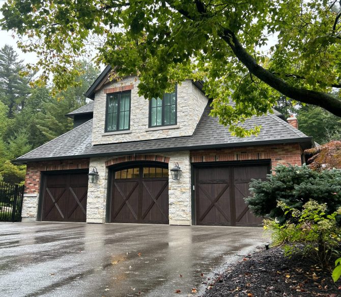 Three dark wood carriage-style garage doors on a luxury stone and brick home.