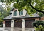 Three dark wood carriage-style garage doors on a luxury stone and brick home.