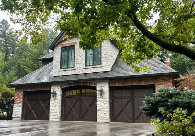 Three dark wood carriage-style garage doors on a luxury stone and brick home.