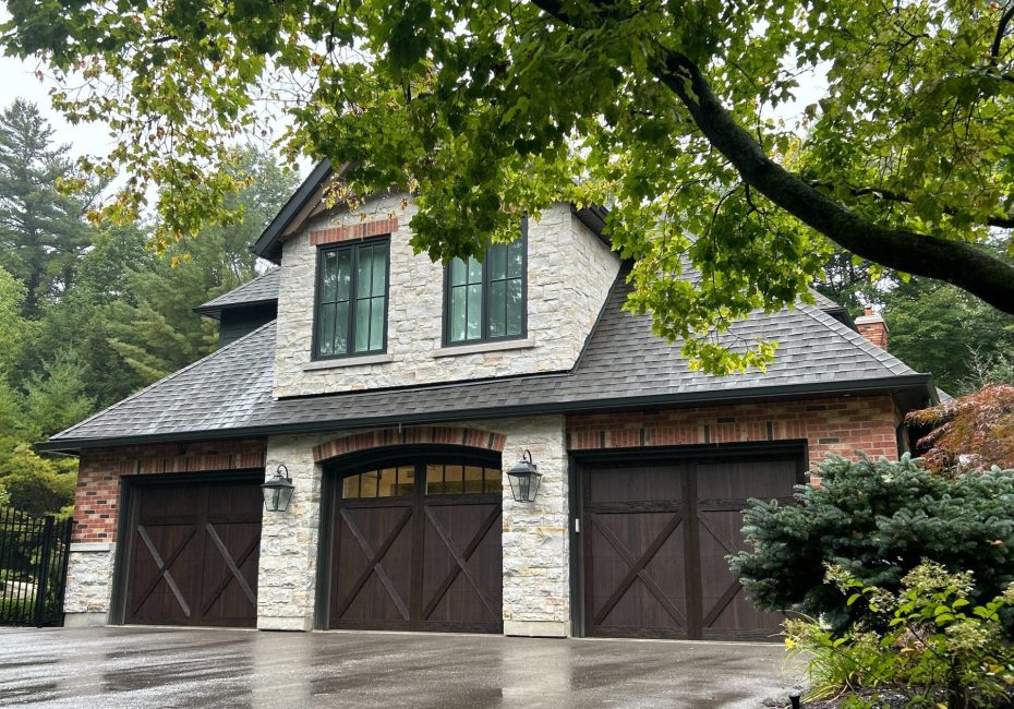 Three dark wood carriage-style garage doors on a luxury stone and brick home.