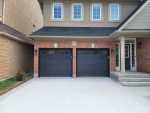 Pair of modern double garage doors with top-panel tinted windows installed by Dodds Garage Doors on a red brick suburban home with a concrete driveway.