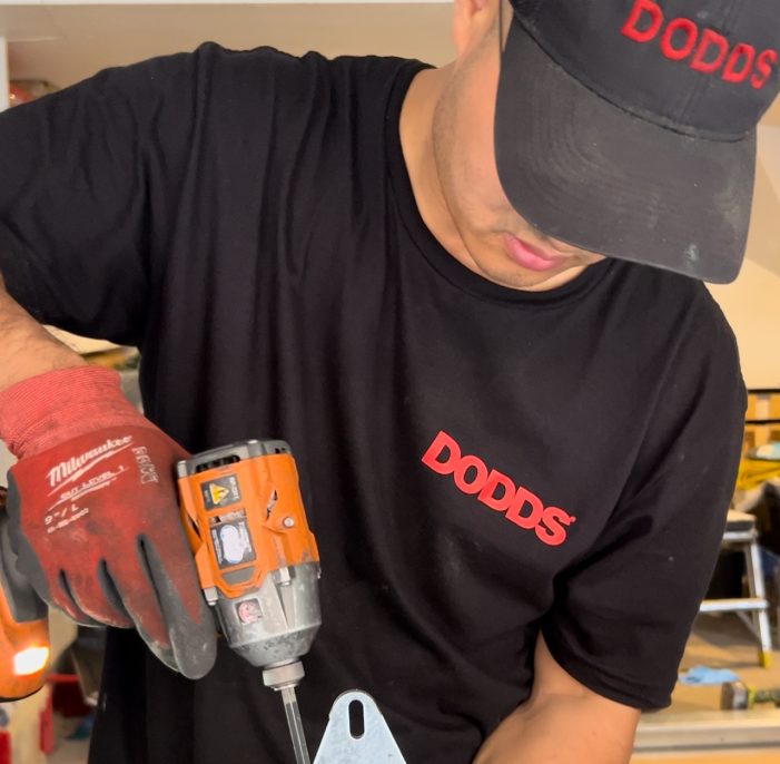 A Dodds Garage Doors technician repairing a garage door track for a customer in Newmarket, wearing a branded Dodds uniform.