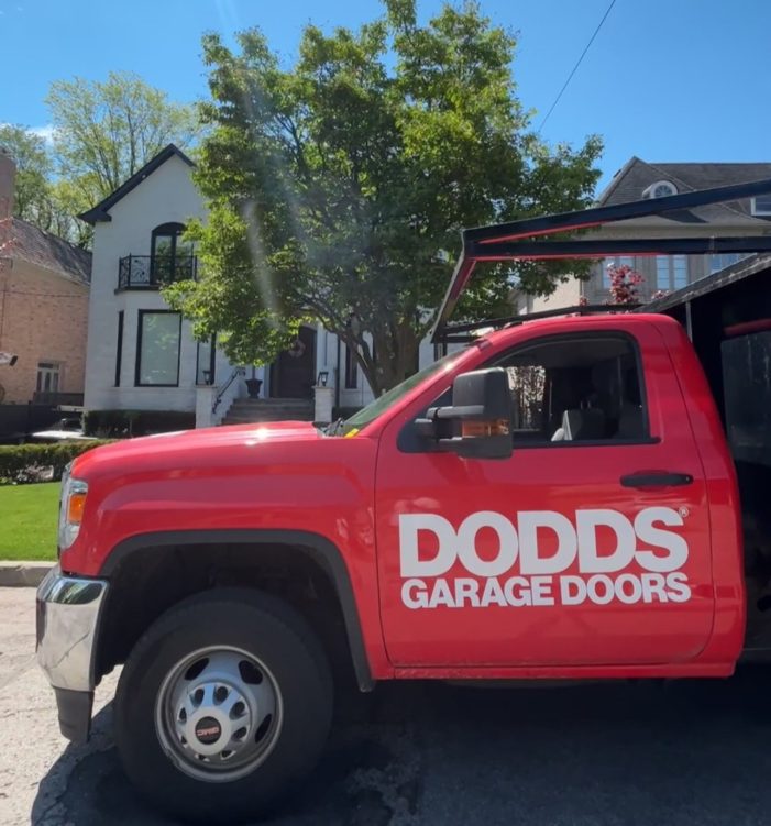 A red Dodds Garage Doors service truck parked in a Maple neighborhood for a residential repair appointment.