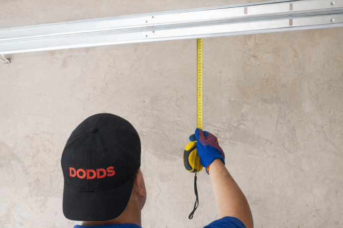 A Dodds Garage Doors technician in a branded hat taking precise measurements for a new door installation in Ajax.
