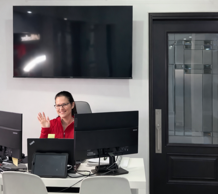 Friendly Dodds Garage Doors customer service representative waving from the Mississauga office desk under the company logo.