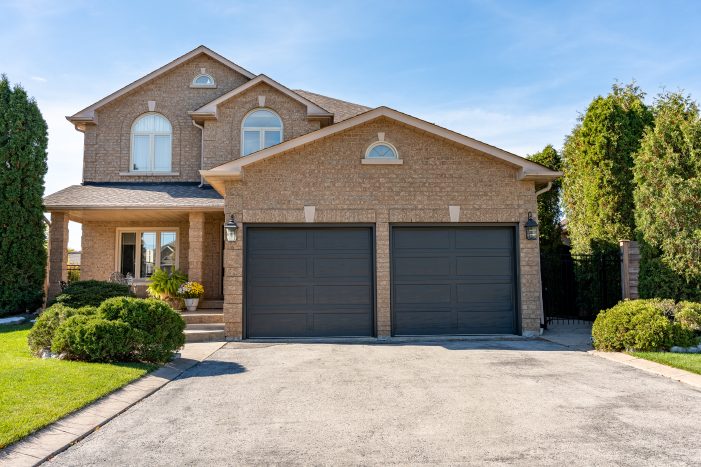 A beautiful brick home in Maple, Ontario, featuring a professional double garage door replacement with dark contemporary panels.