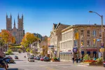 A sunny day on Wyndham Street in downtown Georgetown, Ontario, showing historic stone buildings, local shops, and the Basilica of Our Lady Immaculate in the background.