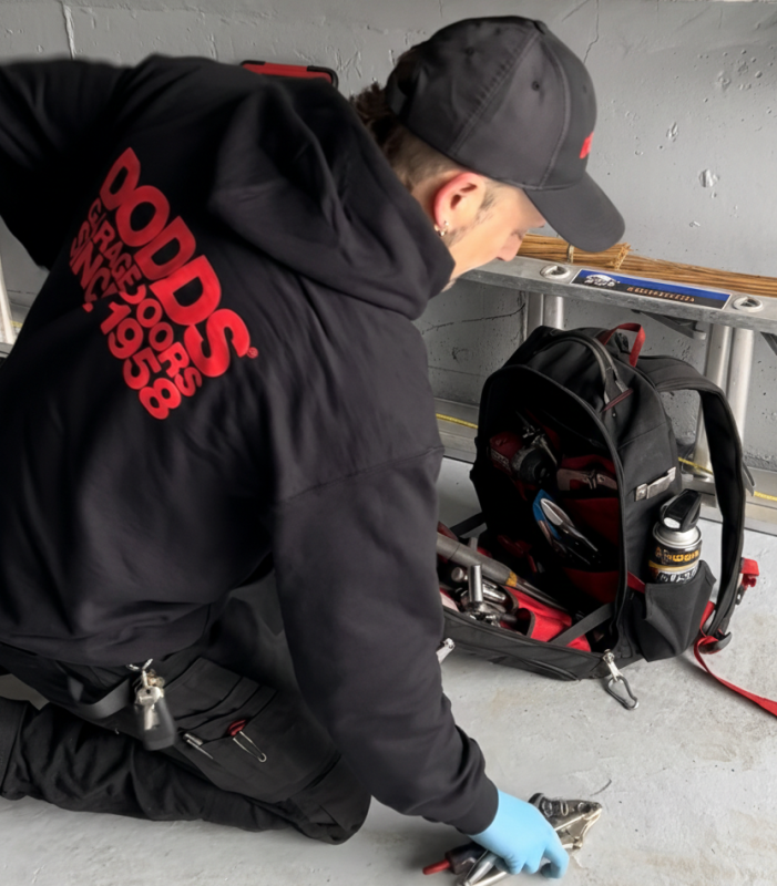 Professional garage door technician from Dodds Garage Doors performing maintenance and organizing tools in a residential garage.