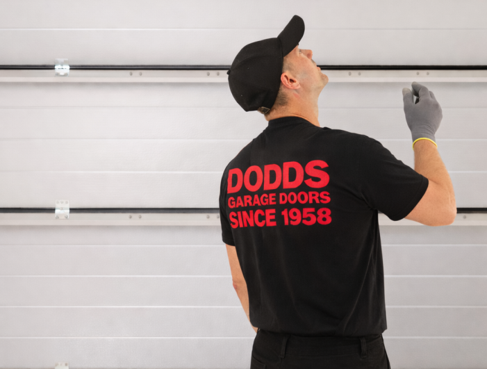 A professional Dodds Garage Doors technician inspecting a white sectional garage door during a repair.