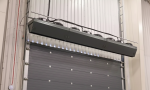 A black heavy-duty commercial air curtain with visible intake fans installed above a metal ribbed warehouse exterior door.