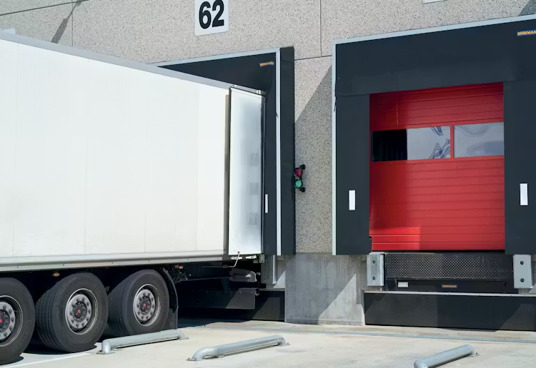 White semi-truck backed into a warehouse loading bay equipped with black dock seals and heavy-duty rubber dock bumpers for wall protection.