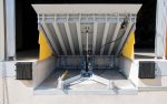 Under-deck view of a heavy-duty mechanical dock leveler showing the lifting mechanism and yellow safety toe guards at a loading bay.