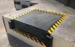 A heavy-duty hydraulic dock leveler with yellow safety stripes installed at a warehouse loading bay by Dodds Garage Doors.