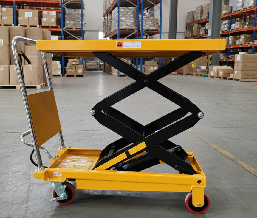 Side view of a yellow manual scissor lift table in a logistics facility, demonstrating the elevated platform height for ergonomic warehouse operations.