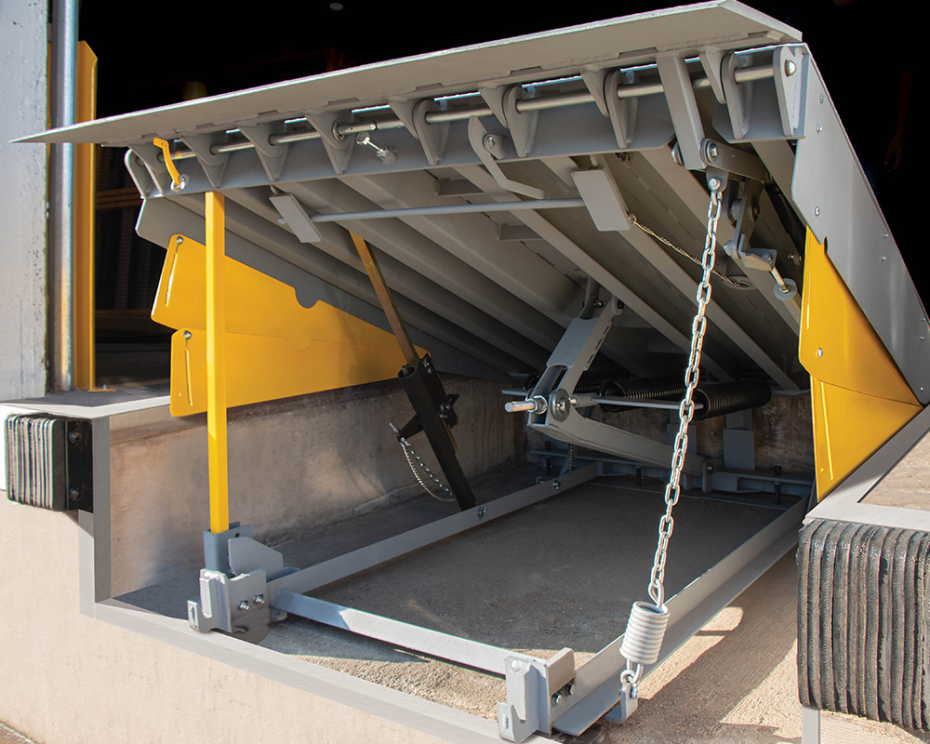 Under-deck view of a heavy-duty mechanical dock leveler showing the lifting mechanism and yellow safety toe guards at a loading bay.
