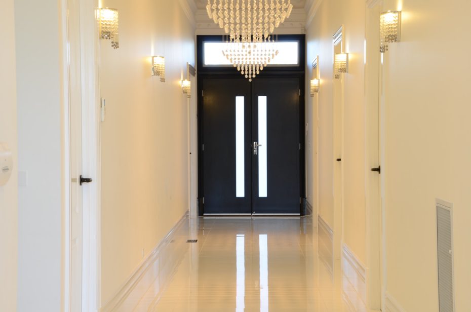Interior view of a modern black steel entry door with vertical glass inserts and a luxury chandelier.