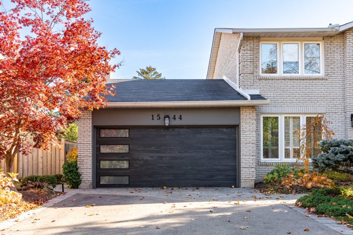A modern charcoal grey garage door with vertical windows installed on a brick home in Ajax.