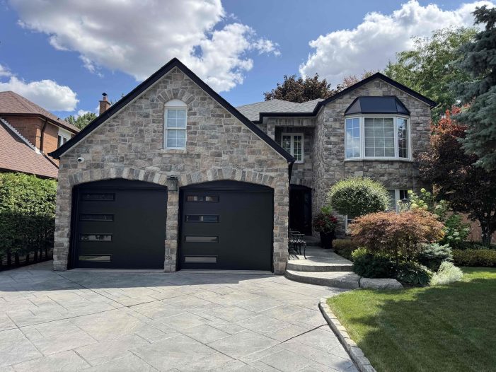 Modern black garage doors with horizontal windows installed on a stone house in Oakville.