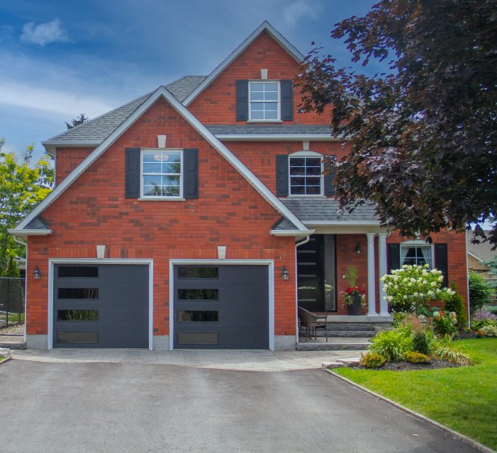 Contemporary red brick home in Bolton featuring two modern black garage doors with horizontal glass inserts.