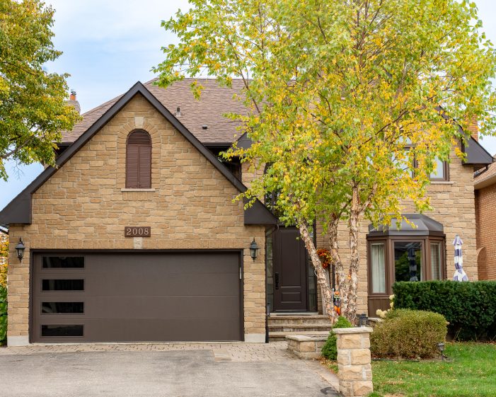 A modern brown flush-panel garage door with vertical windows installed on a stone house.