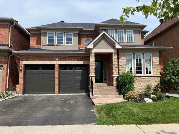 Custom black double garage doors installed on a brick residential home in Scarborough, Ontario.