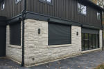 Sleek black security roll shutters installed on a modern stone and wood-sided home for maximum privacy and weather protection.