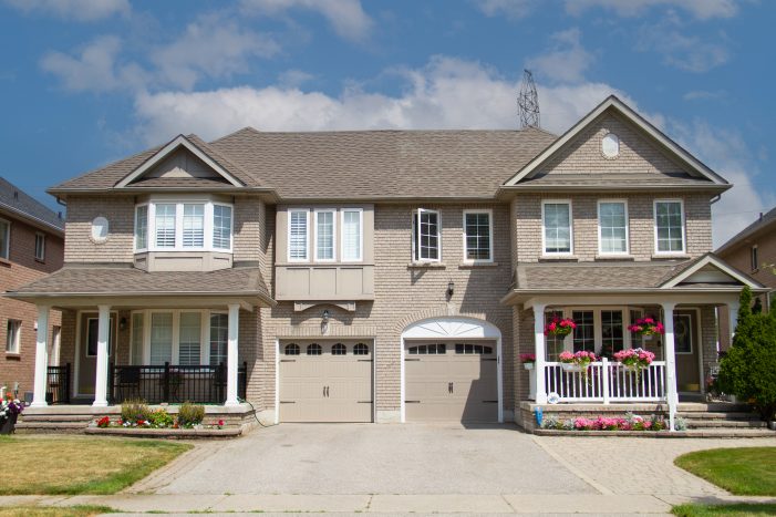 A brick semi-detached home in Newmarket featuring two classic tan garage doors installed by Dodds Garage Doors.
