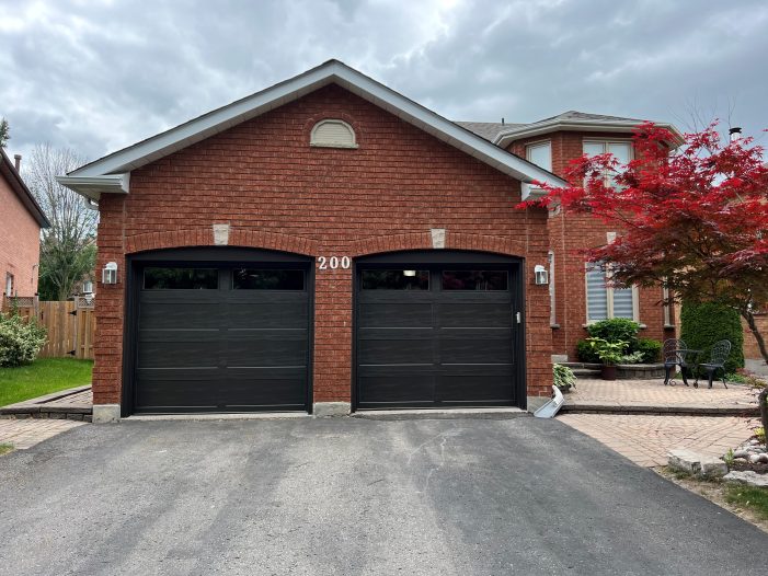 Modern black double garage doors installed on a brick home in a Kingston, Ontario neighborhood.