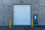 Pair of yellow steel safety bollards installed to protect a commercial overhead garage door from vehicle impact.