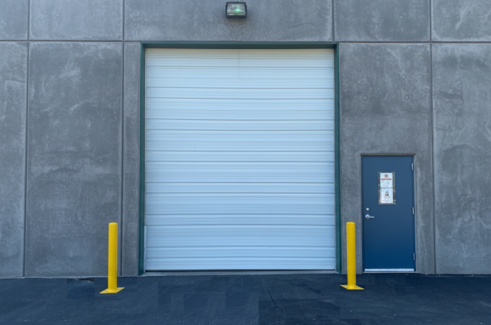 Pair of yellow steel safety bollards installed to protect a commercial overhead garage door from vehicle impact.