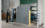 An operator using a wall-mounted control panel to safely deploy a vertical dock leveler for trailer loading at a distribution hub.