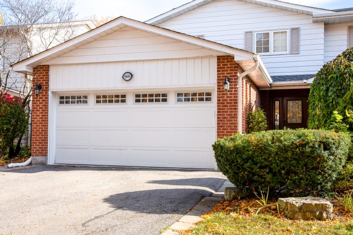 New installation of a white sectional garage door with windows on a brick-front Orillia home (near lake Simcoe), showcasing improved curb appeal.