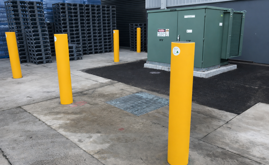 High-visibility yellow industrial safety bollards protecting electrical equipment in a warehouse loading area.