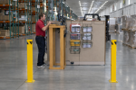 Two high-visibility yellow steel safety bollards installed on a warehouse floor to protect a workstation and personnel from forklift traffic.