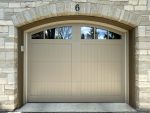 Close-up of a custom beige garage door with arched windows installed under a stone archway by Dodds Garage Doors.