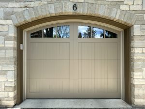 Close-up of a custom beige garage door with arched windows installed under a stone archway by Dodds Garage Doors.