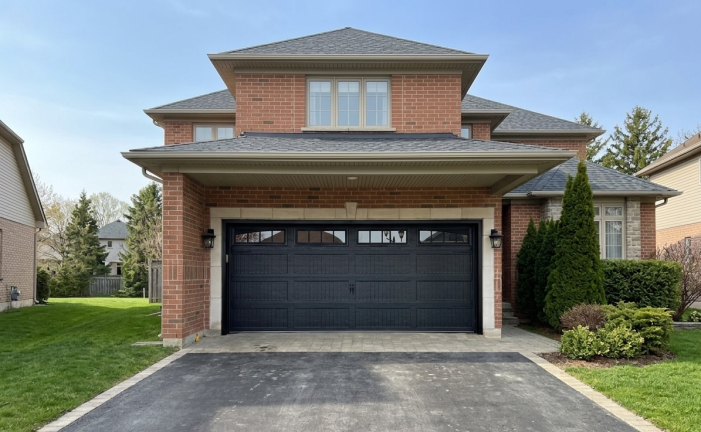 Wide exterior view of a brick home featuring a black recessed long panel coach garage door in Caledon East