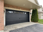 Right-side angle view showing a black recessed long panel garage door with decorative hardware and interlocking driveway