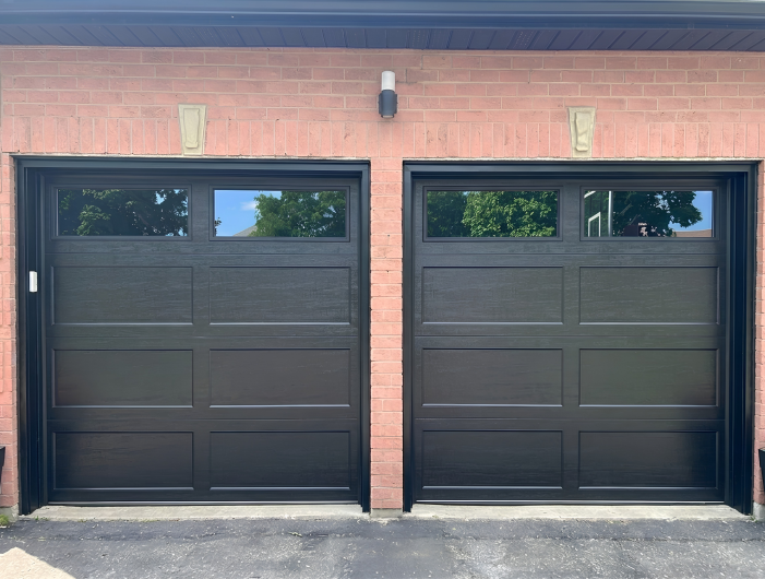 Close-up front view of two black recessed long panel garage doors featuring dark tinted double-glazed windows and black weatherstripping.