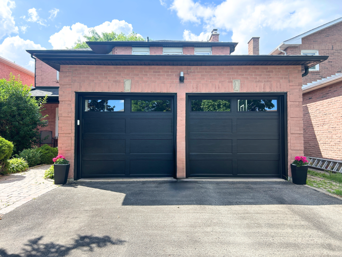 Straight-on full front view of two black recessed long panel insulated garage doors installed on a red brick home in Richmond Hill.