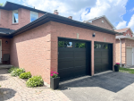 Side-angle view showing two modern black recessed long panel garage doors with dark tinted top windows installed by Dodds Garage Doors in Richmond Hill.