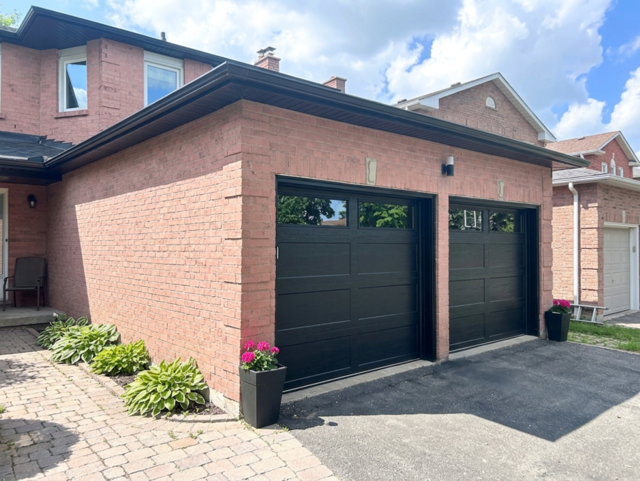 Side-angle view showing two modern black recessed long panel garage doors with dark tinted top windows installed by Dodds Garage Doors in Richmond Hill.