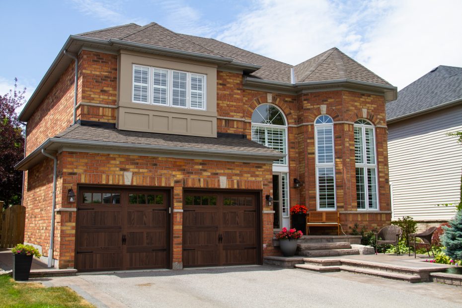 Angle view of a brick home in Whitby, Ontario after a complete carriage house garage door replacement in dark oak.