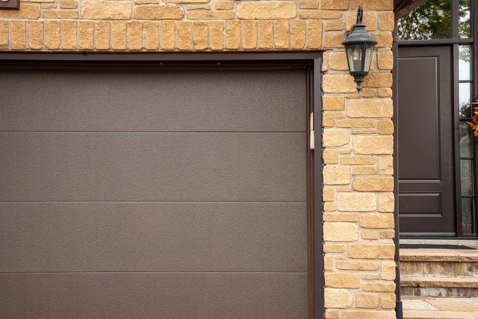 Close-up details of the textured finish on a modern brown flush garage door panel next to stone brickwork.