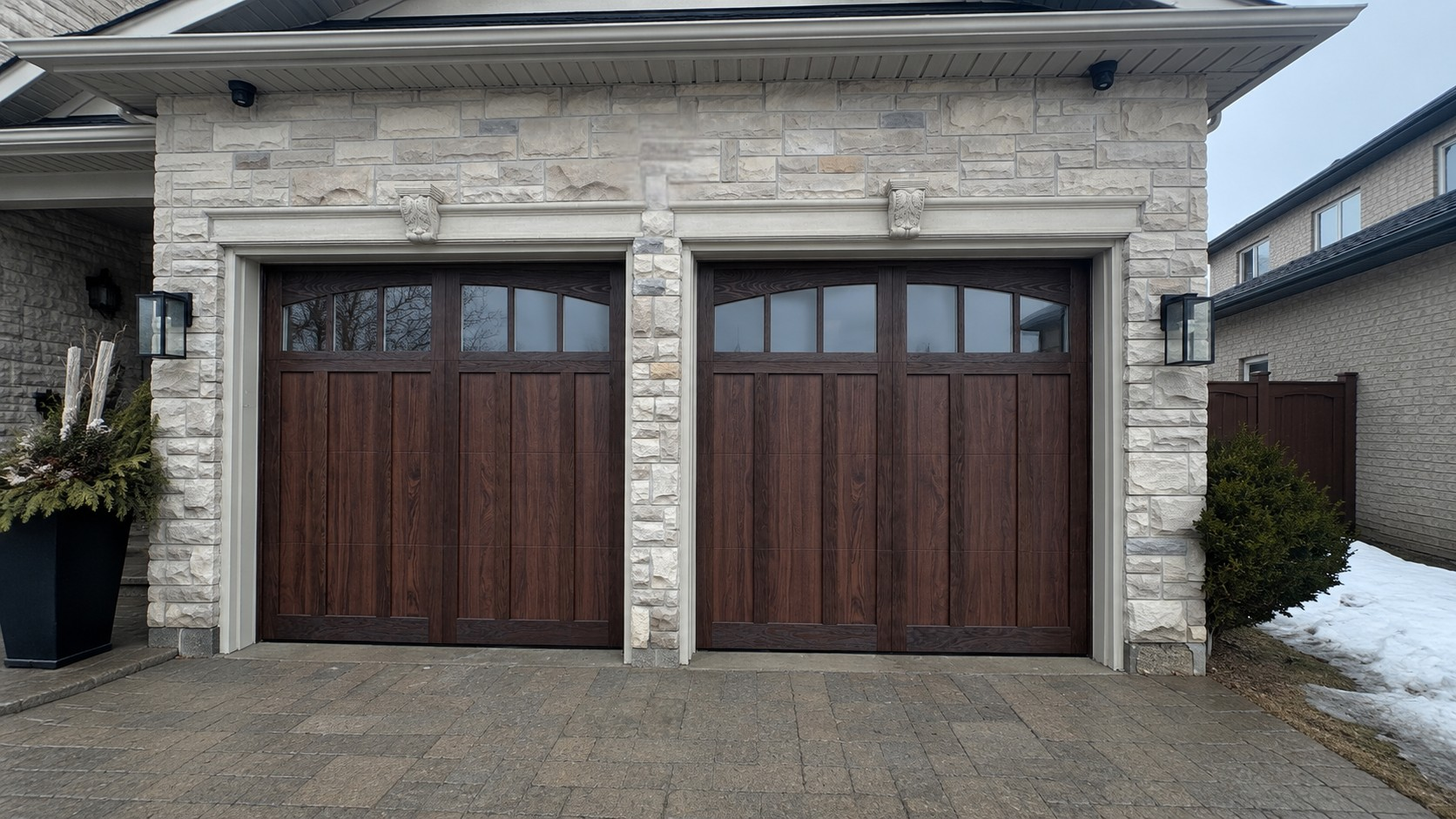 New dark wood-grain carriage style garage doors with arched glass windows installed on a stone home in Woodbridge, Ontario.