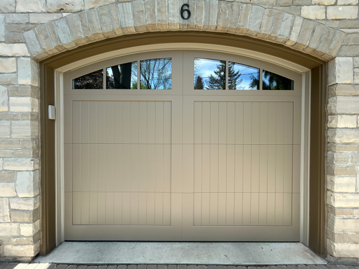 Symmetrical view of a closed custom steel wood overlay garage door framed perfectly by a stone arch.