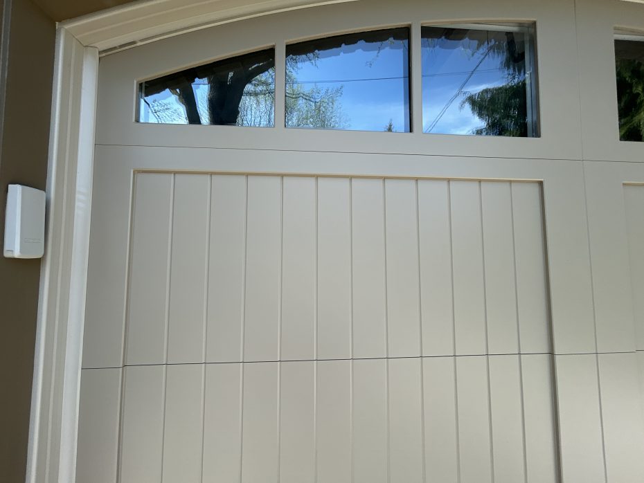 Close-up of arched top windows on a custom steel wood overlay garage door reflecting a blue sky.