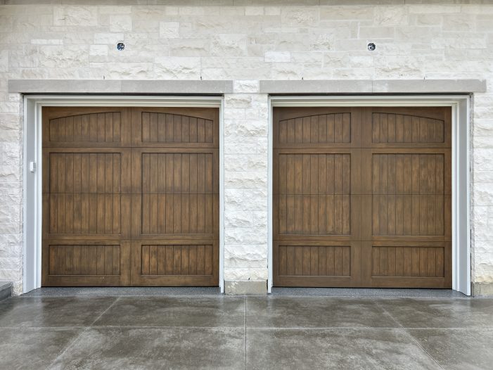 Full exterior of a modern white brick and stone custom home featuring two steel wood overlay garage doors.
