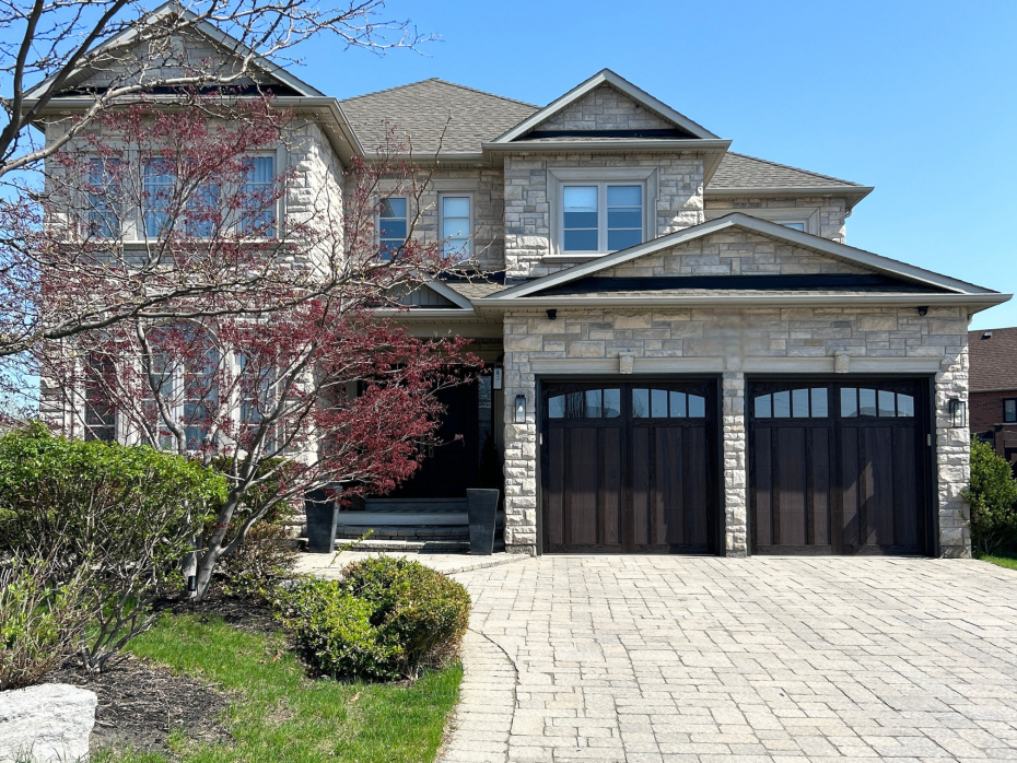 Walnut carriage style garage doors with arched glass windows installed on a stone home in Woodbridge, Ontario.
