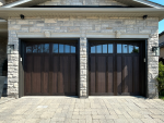 Straight-on view of newly installed dark wood-grain carriage style garage doors on a stone home in Woodbridge, Ontario.